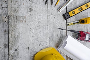 Top view construction tools such as a yellow hard hat, spirit level, measuring tape, folding ruler arrayed against a wooden plank