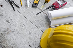 Top view construction tools such as a yellow hard hat, spirit level, measuring tape, folding ruler arrayed against a wooden plank