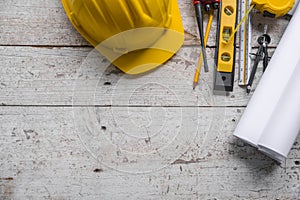 Top view construction tools such as a yellow hard hat, spirit level, measuring tape, folding ruler arrayed against a wooden plank