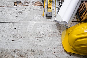 Top view construction tools such as a yellow hard hat, spirit level, measuring tape, folding ruler arrayed against a wooden plank