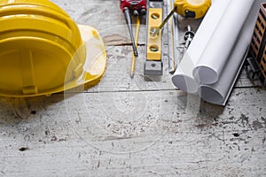 Top view construction tools such as a yellow hard hat, spirit level, measuring tape, folding ruler arrayed against a wooden plank