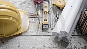 Top view construction tools such as a yellow hard hat, spirit level, measuring tape, folding ruler arrayed against a wooden plank