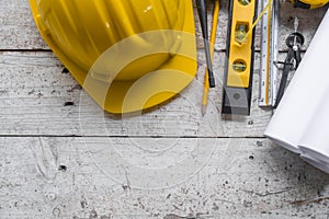 Top view construction tools such as a yellow hard hat, spirit level, measuring tape, folding ruler arrayed against a wooden plank