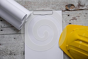 Top view construction tools such as a yellow hard hat, spirit level, measuring tape, folding ruler arrayed against a wooden plank