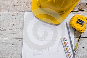 Top view construction tools such as a yellow hard hat, spirit level, measuring tape, folding ruler arrayed against a wooden plank