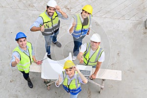 Top view of contractors, engineers and formats team in safety vests with helmets working with laptops, standing on under-