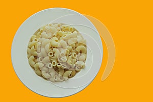 Top view cooked macaroni on white round plate and background is bright yellow.