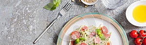 Top view of cooked Pappardelle with tomatoes, basil and prosciutto near ingredients and fork on grey surface, panoramic shot