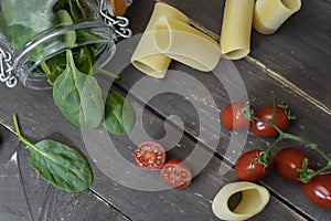 Top view of cooking italian pasta ingredients.Fresh spinach leaves in jar, cherry tomato and raw tube penne.Healthy nutrition food