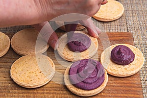 Top view of Cooking macarons cookies at home. Female hand squeezes cream on homemade cookie