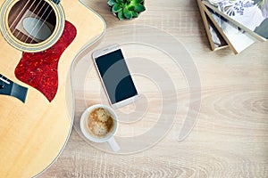 Top view of cosy home scene. Guitar, books, cup of coffee, phone and succulent plants over wooden background. Copy space, mock-up