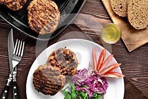 Top view of country dinner with cutlet and fresh salad, brown bread and moonshine on wooden table