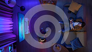 Top view of couple arguing in the apartment living room, man on the couch playing game on TV in VR glasses.