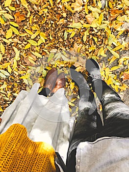 Top view of couples feet in yellow autumn leaves. Stylish hipster couple legs in fall leaves in sunny warm city street. Traveling