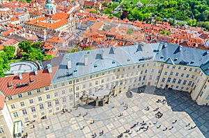 Top view of courtyard square of Prague Castle and Old Royal Palace with small figures of walking people tourists, red tiled roof