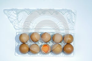 Top view of cracked fresh egg and whole eggs with bright yolk in plastic tray for eggs.