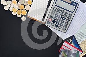 Top view of credit cards, passbooks saving account, calculator, notepad with pen and pile of coins on black background