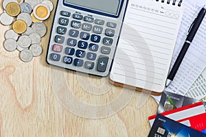 Top view of credit cards, passbooks saving account, calculator, notepad with pen and pile of coins on wood background, copy space