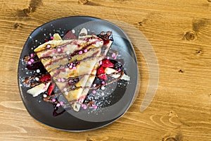 Top view of crepe with chocolate cream, chocolate chips, banana and strawberry served on grey plate