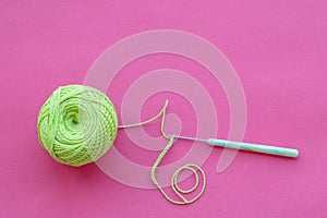 Top view on crochet hook and green jute thread ball on a pink background with copy space. Eco-friendly knitting