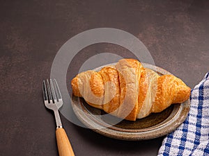 Top view of croissant milk on a plate, cutlery, and a cloth placed on the old kitchen table.