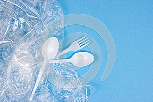 Top view of crushed plastic spoons, forks, bottles and cups as a disposable waste with copy space on bright blue background