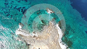 Top view of crystal clear water rolling on deserted rocky coast. Aerial view of transparent waves of Cyprus