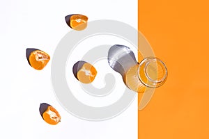 Top view crystal glass with orange juice on white and orange background, four orange segments on the white, horizontal