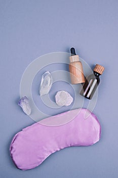 Top view of crystals gemstones minerals, violet purple eye pillow, glass and wooden bottles for essential oils over grey