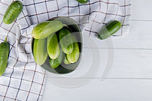 top view of cucumbers in bowl with other ones on plaid cloth and wooden background