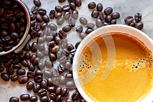 Top view of a cup of American coffee with a nice crema on the top on a concrete table with a pile of organic arabica coffee beans