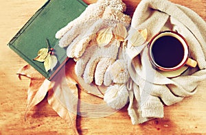 Top view of Cup of black coffee with autumn leaves, a warm scarf and old book on wooden background. filreted image