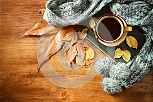 Top view of Cup of black coffee with autumn leaves, a warm scarf and old book on wooden background. filreted image.