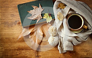 Top view of Cup of black coffee with autumn leaves, a warm scarf and old book on wooden background. filreted image