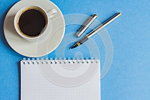 Top view of cup of black coffee with notebook and pen on blue background. business concept with copy space