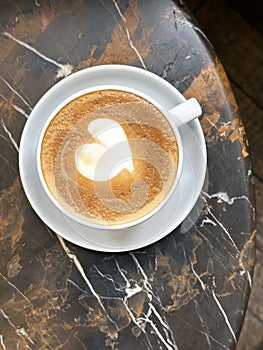 Top view of cup of cappuccino coffee with latte art on marble table