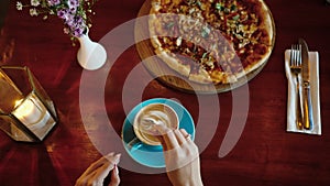 Top view of a cup of cappuccino with foam being stirred with spoon by woman hand