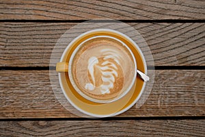 Top-view of a cup of cappuccino with latte art at the midpoint of a wooden table