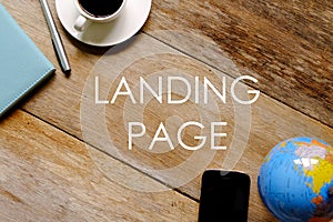 Top view of a cup of coffee,mobile phone,globe,pen and notebook on wooden background written with LANDING PAGE