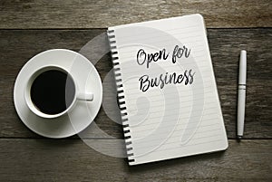 Top view of a cup of coffee,pen and notebook written with ` Open for Business ` on wooden background