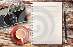 Top view cup of coffee,retro camera,pencil and blank paper on wooden table background. Coffee on office desk. Food and drink