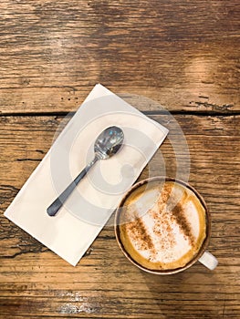 Top view of a cup of coffee with a spoon on a napkin on a wooden table