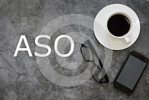 Top view of a cup of coffee, sunglasses and mobile phone on grey floor background written with ASO