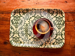 Top view of cup of coffee on vintage floral tray on wooden table