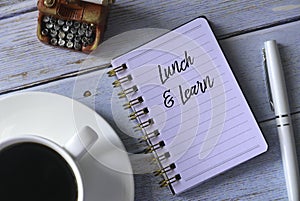 Top view of a cup of coffee,vintage toy typewriter,pen and notebook written with Lunch and Learn on wooden background