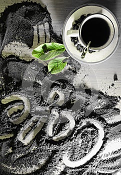 Top view on cup of hot black coffee with green leaves and text word hand written in french `cafÃ©` in milled coffee texture