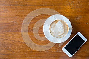Top view of a cup of hot coffee and smartphone put on old wooden