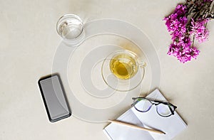 Top view cup of tea with flower , cell phone, glass of water and