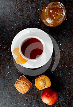 top view of cup of tea with raisins on teabag and peaches cupcake peach jam on black and brown background