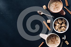 top view of cups of coffee, spoons, bowl of cane sugar and cinnamon stick